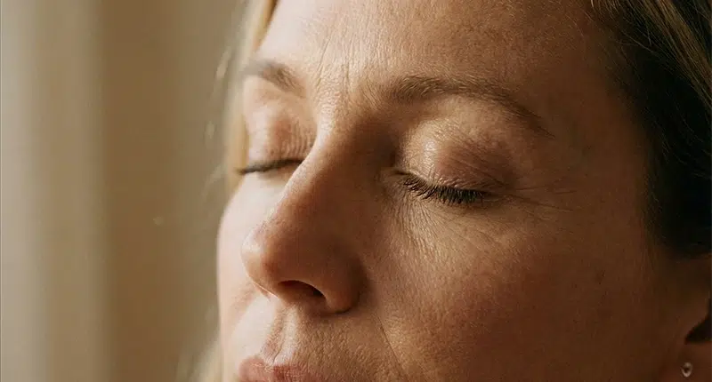 Como o silêncio ajuda a ouvir a sua espiritualidade 2 Close de rosto feminino de olhos fechados, ilustrando uma pausa consciente no dia a dia.