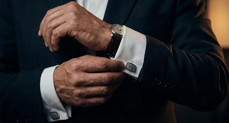 Detalhe das mãos de um homem de negócios ajustando abotoaduras do terno, representando preparação e competência.