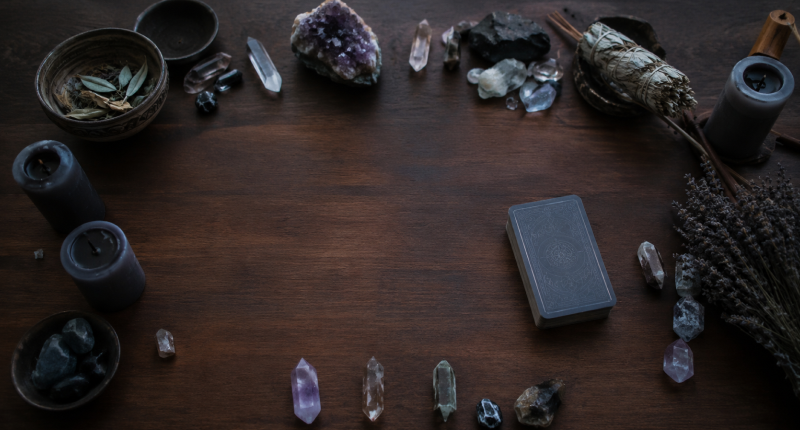 Altar com velas apagadas e baralho fechado sobre mesa de madeira com luz fria, representando o burnout espiritual e a perda de prazer nas práticas espirituais.