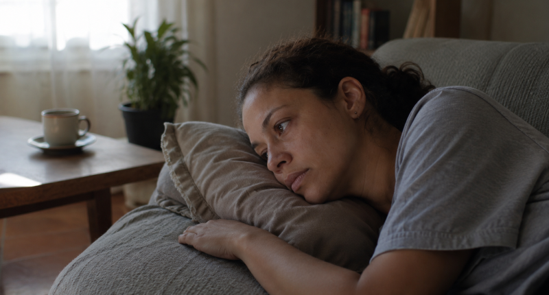 3 sinais de que você está em burnout espiritual e o que fazer 2 Mulher deitada no sofá com olhos abertos fixos no vazio e xícara de chá fria ao fundo, representando a irritabilidade e tristeza persistentes que não respondem às práticas habituais no burnout espiritual.