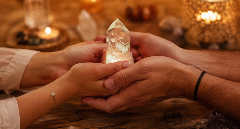 Duas mãos segurando juntas um cristal translúcido sobre mesa de madeira, representando a compatibilidade espiritual como base de um relacionamento amoroso duradouro.